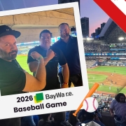 Three men pose for a photo in a polaroid frame at a baseball stadium during a BayWa re Baseball Game, with APsystems logo nearby.