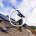 Two workers install solar panels on a sloped residential roof under a blue sky with clouds.