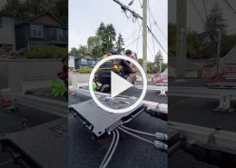 Video thumbnail: two utility workers in safety gear on a platform atop a truck, working on overhead power lines in a suburban street.