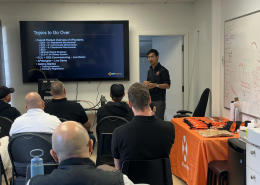Instructor presenting a slide titled 'Topics to Go Over' to a group in a training room with a large screen at the frontison.